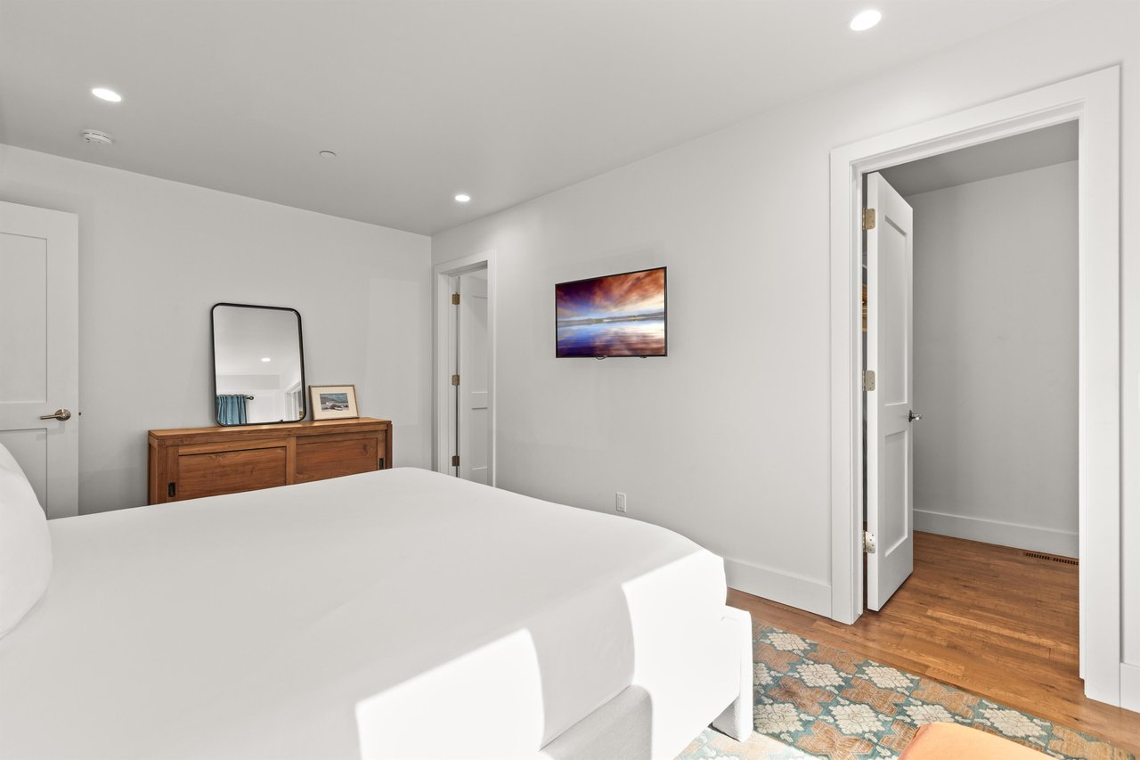 Sink into crisp white linens in your serene bedroom, featuring warm wood floors and thoughtful artwork for peaceful nights.
