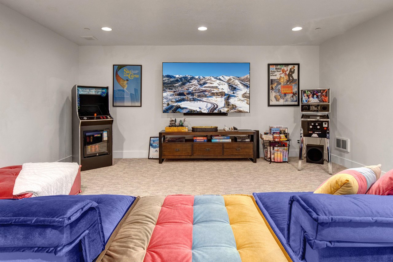 A spacious game room with a colorful sectional seating, arcade games, and numerous board games.