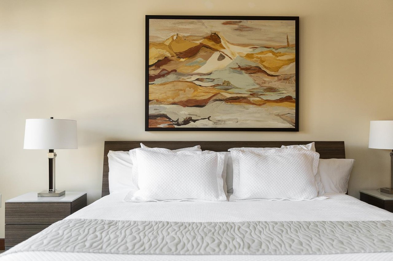 Luxurious king bed in the main suite, white linen and duvet cover with mountain modern art above the wooden headboard