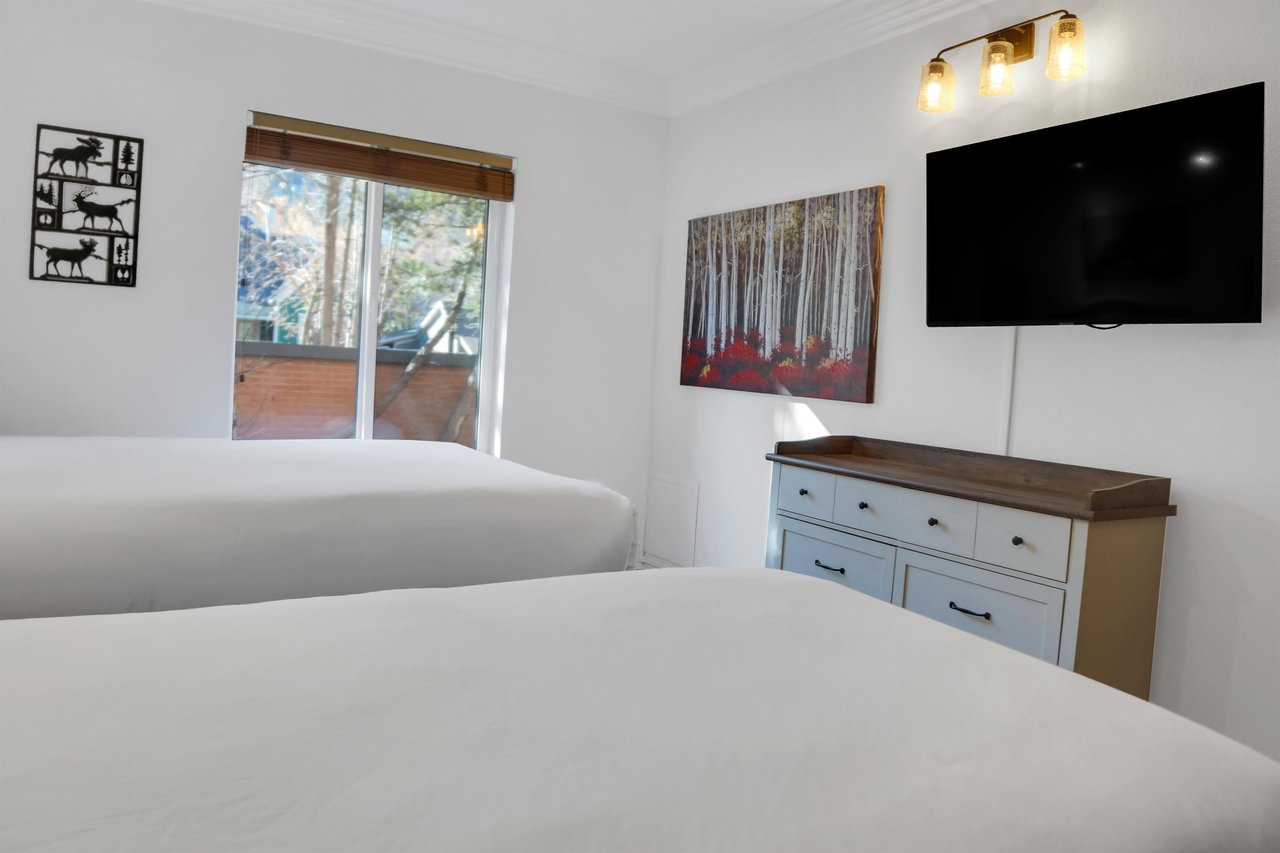 The second bedroom has two twin beds, dresser, and wall mounted TV above the dresser.