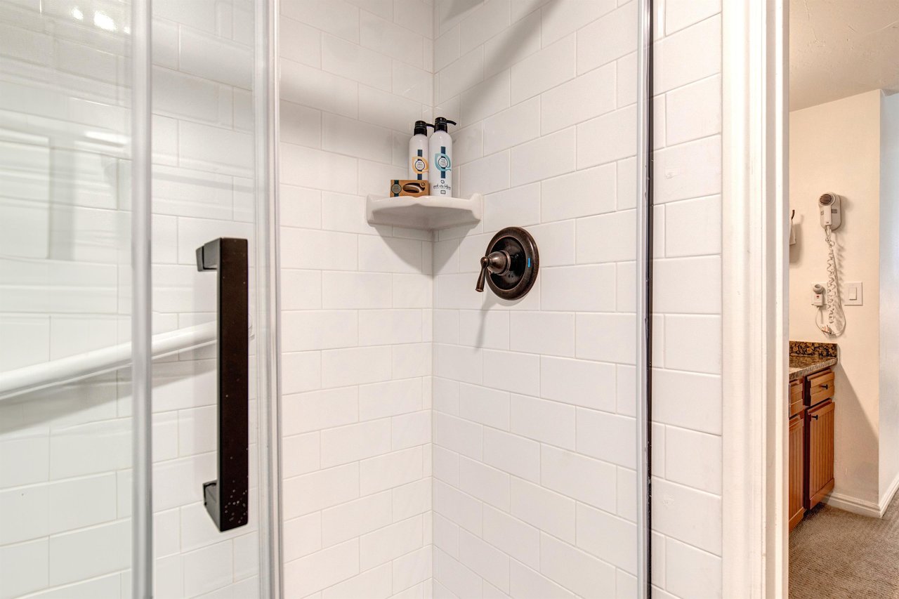 The en suite bathroom has a walk in shower with white tile, glass door, and black hardware.