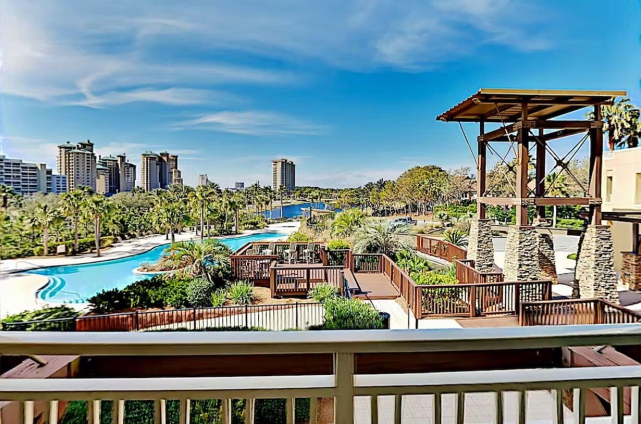The winding lagoon pool nestled between a spacious wooden deck with seating in the foreground and a deepblue lake in the distance