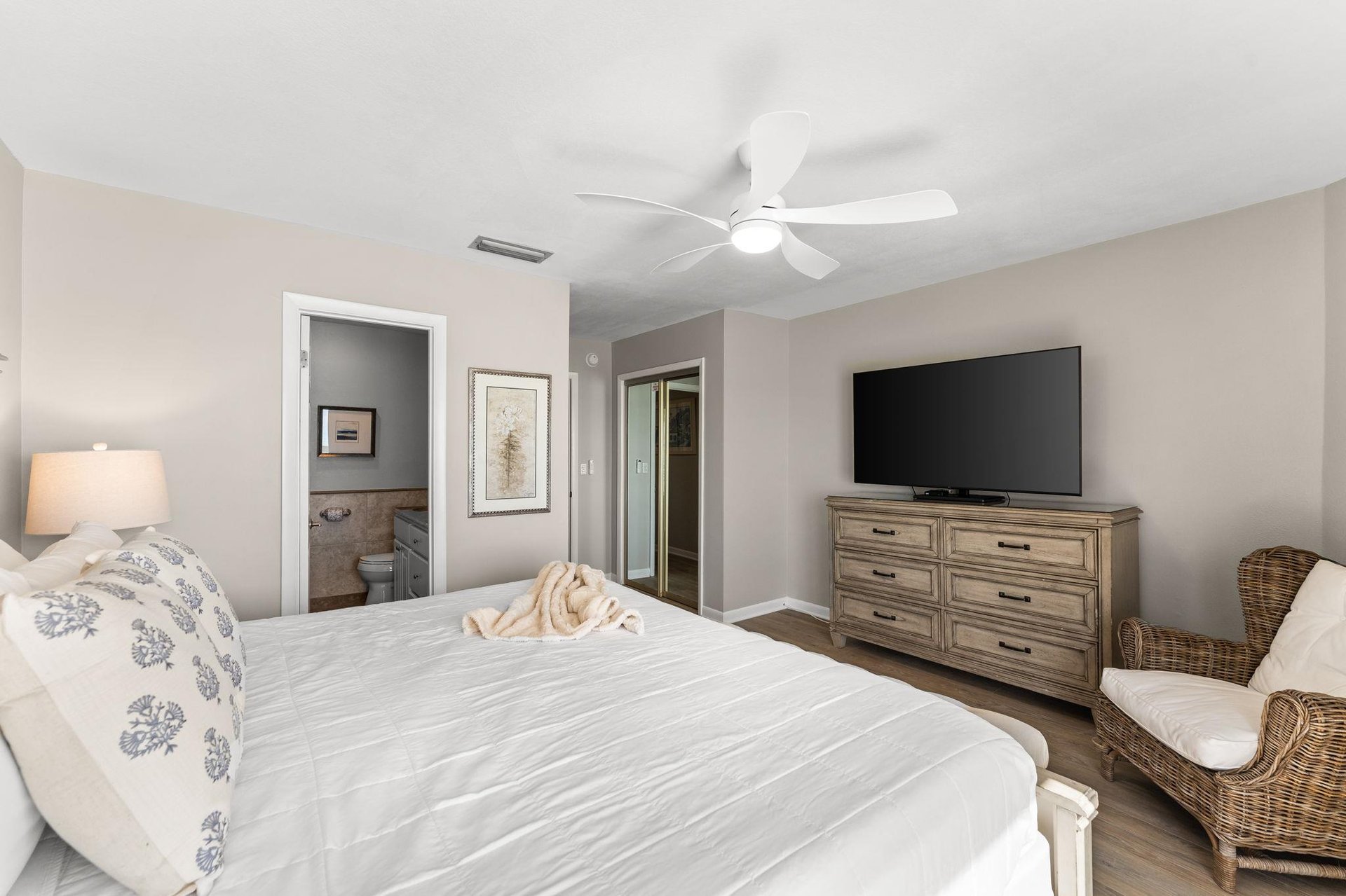 Bedroom 1 offers plush linens, coastal decor, and modern amenities including ceiling fan and flatscreen TV.