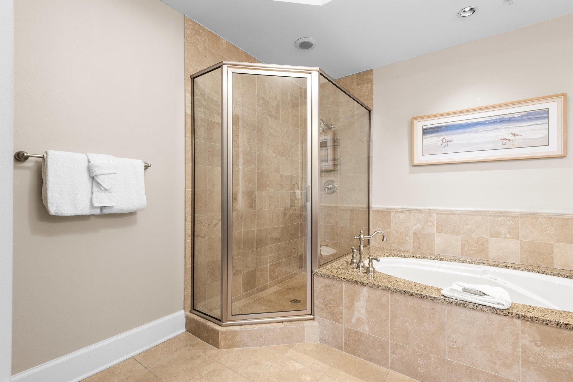 Ensuite spalike bathroom features a spacious glass shower, luxurious soaking tub, and warm travertine finishes for ultimate relaxation.