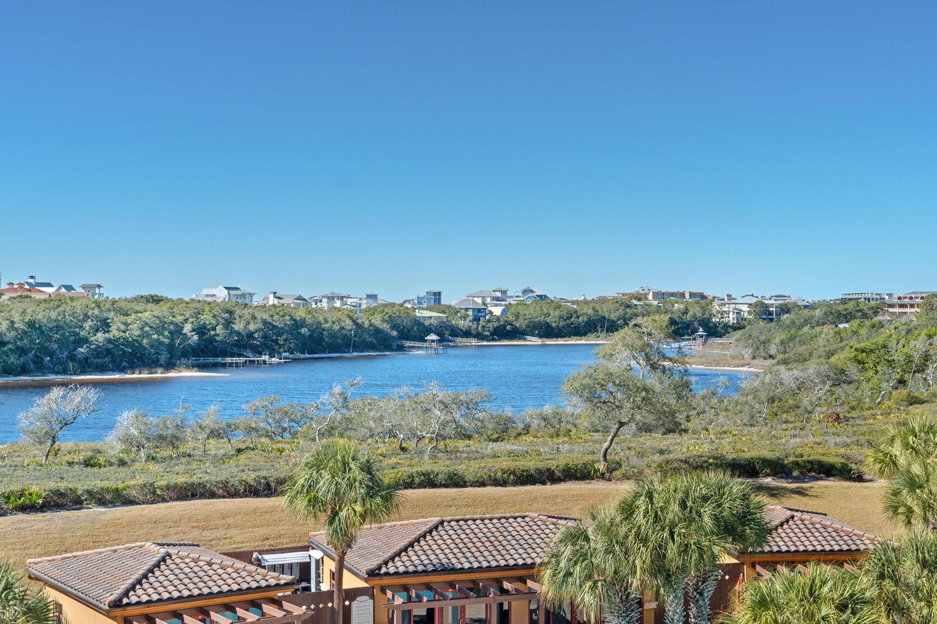 Coastal community nestled among native vegetation along pristine gulf and lake waters under clear blue skies.