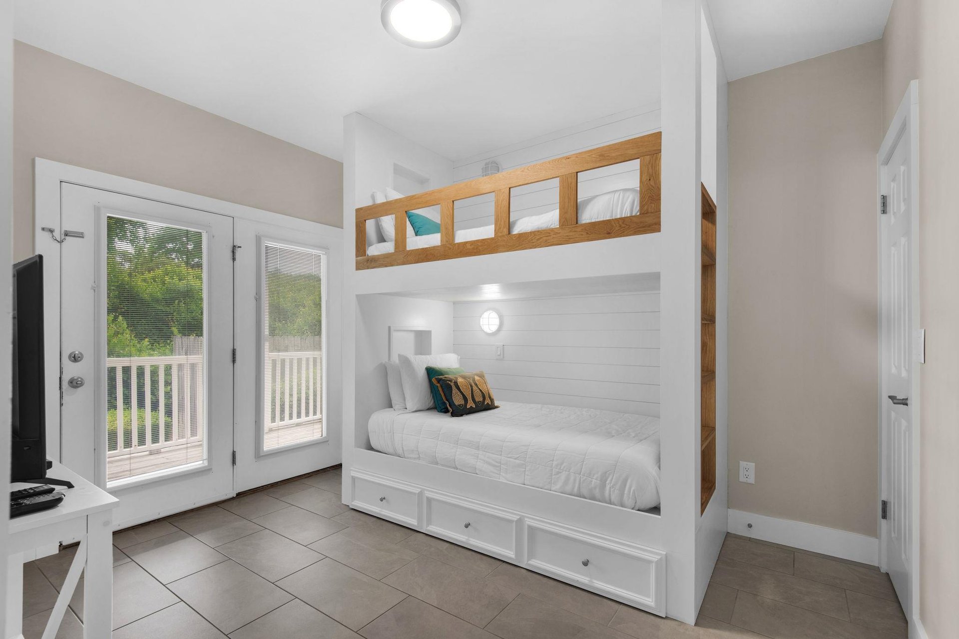 Bedroom 3 1st Fl features custom white shiplap beds with cozy storage drawers, natural light streaming through doors to the deck, and all the restful charm you need after a beach day.