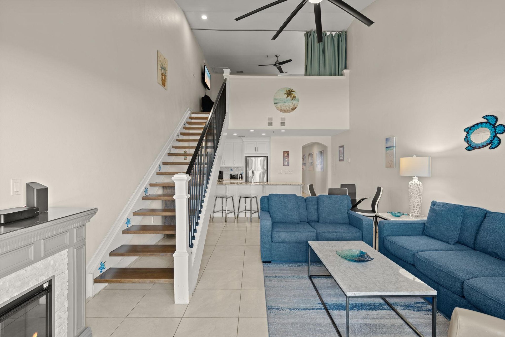 Open loftstyle retreat where soaring ceilings and coastal blues create your perfect escape. Relax on plush seating, enjoy the cozy atmosphere, and let the breezy design transport you to vacation mode