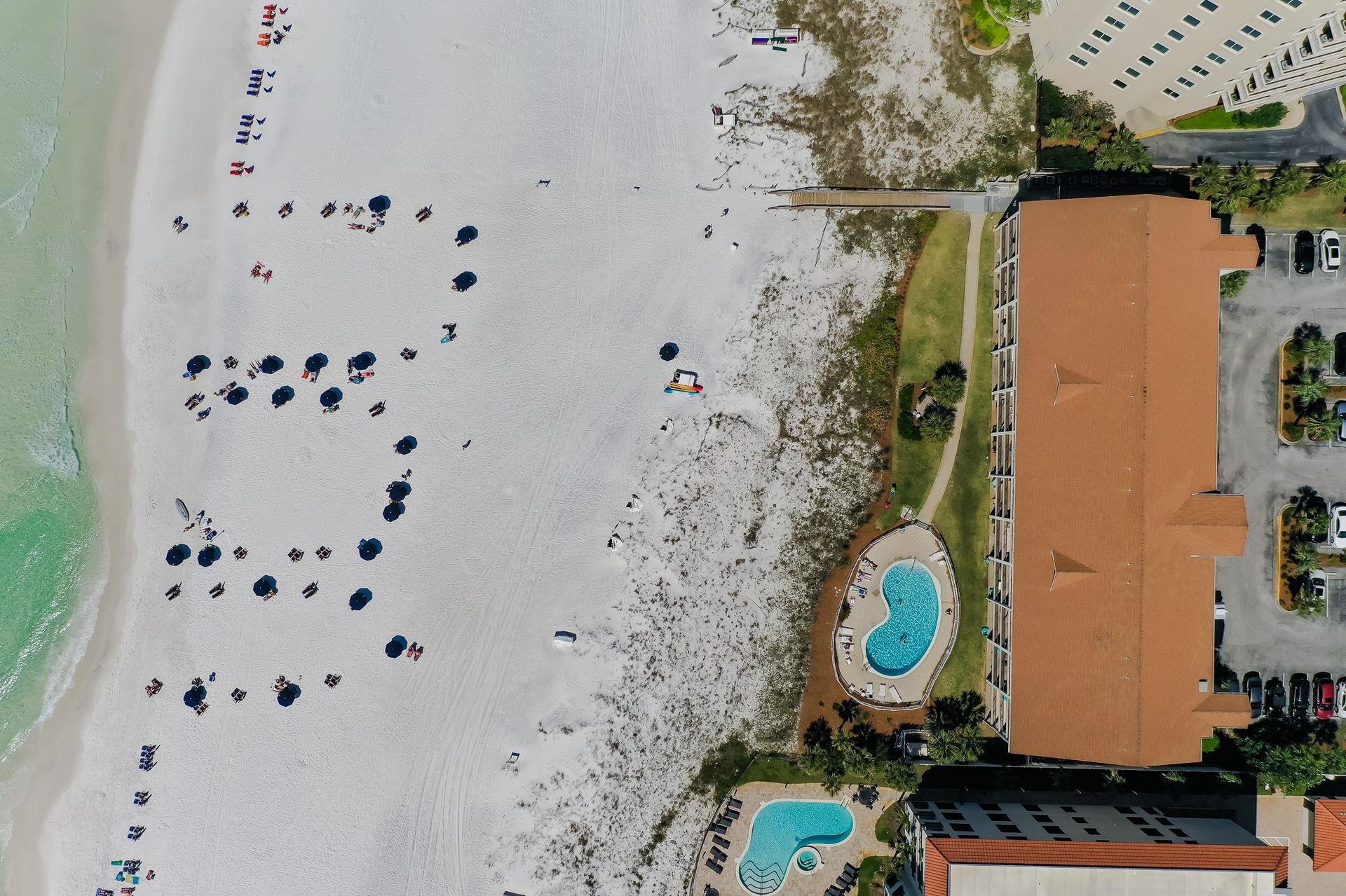 Aerial view of a beachfront property featuring two swimming pools, direct beach access with pristine white sand, and proximity to calm, turquoise waters ideal for relaxation.