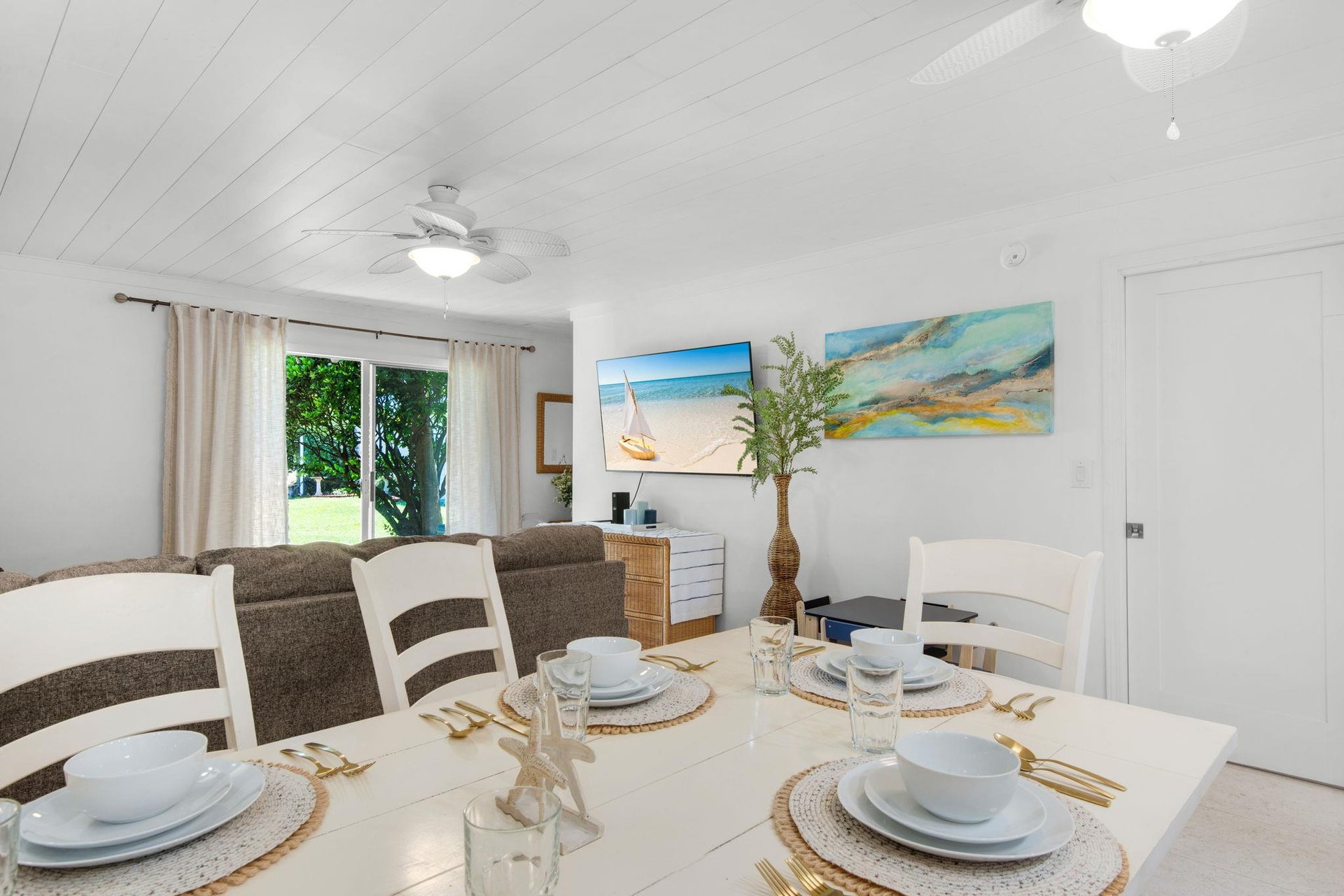 Picture yourself at this dining table set for a meal, with coastal artwork adorning the walls and natural light streaming through to the living area beyond.