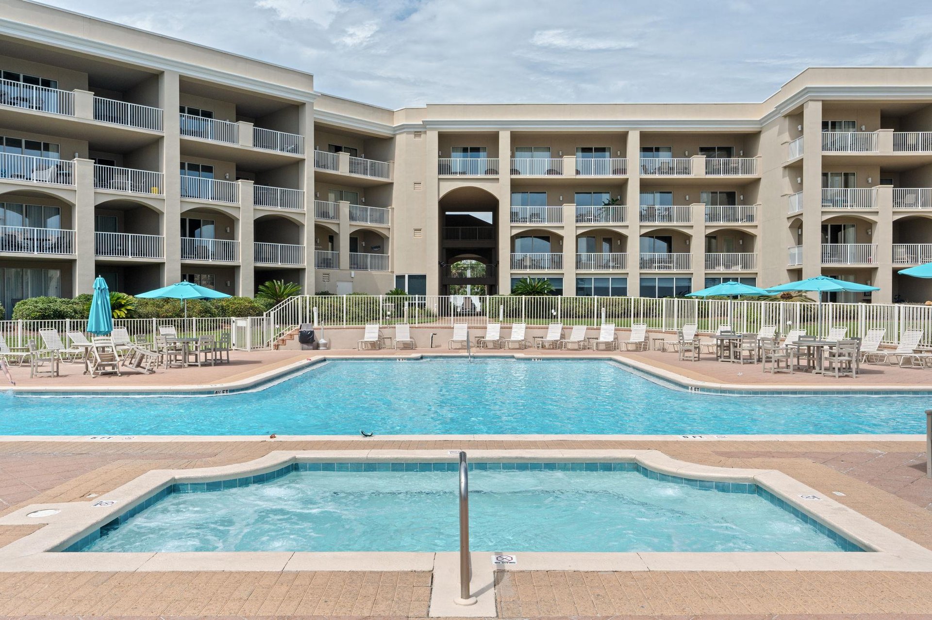 Beachfront resort featuring a sparkling pool, hot tub, and multiple balconies under sunny skies—your coastal retreat awaits.