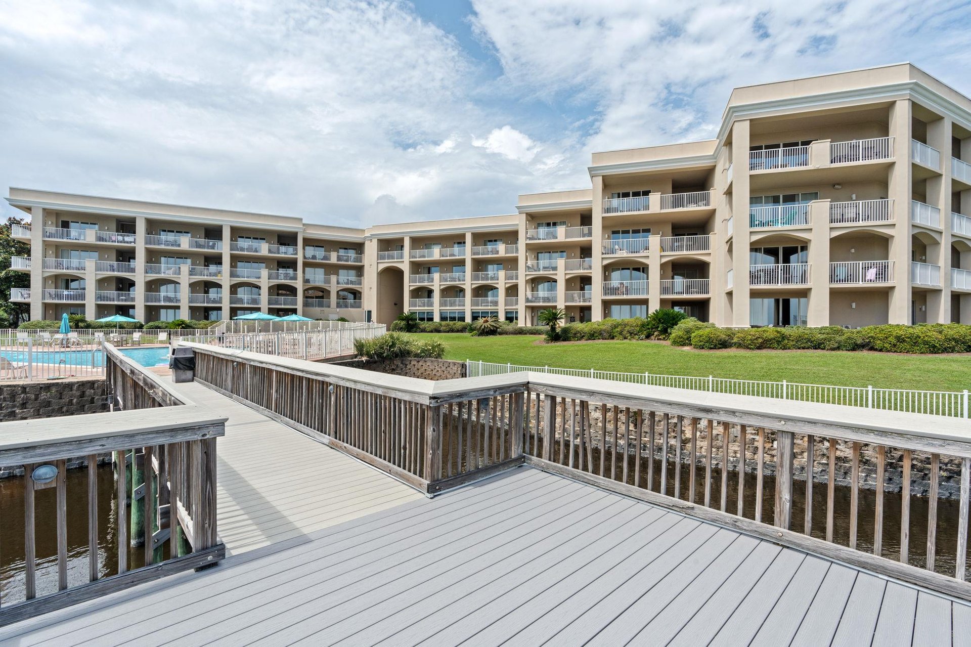 Threestory property features tiered architecture with multiple balconies, manicured lawn, swimming pool, and waterfront access via private boardwalks.