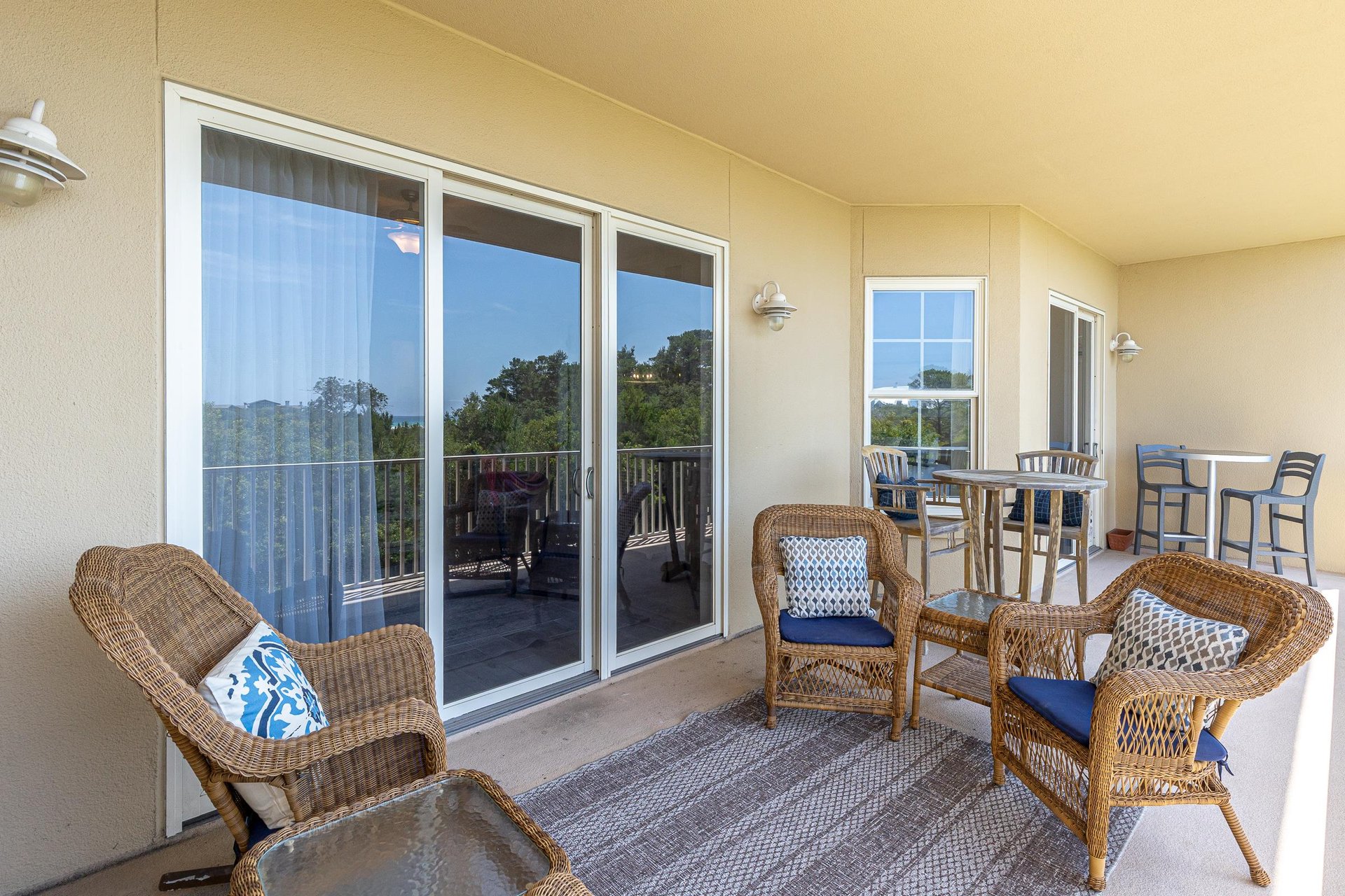 Covered balcony provides a comfortable retreat with wicker seating, bistro table, and peaceful treetop views stretching into the distance.