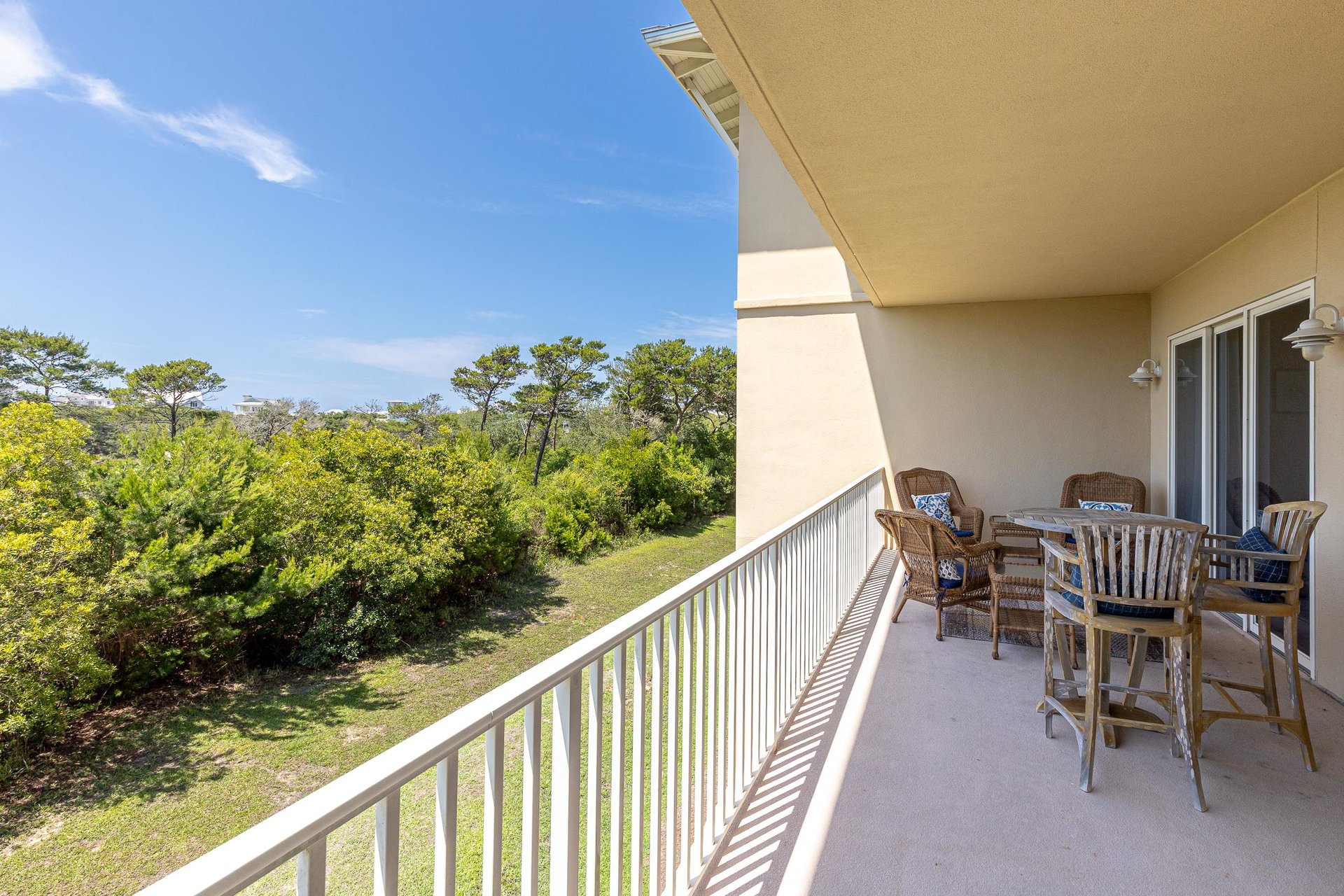 A spacious outdoor terrace overlooks lush coastal greenery under clear blue skies, offering the perfect spot to dine al fresco or simply unwind.