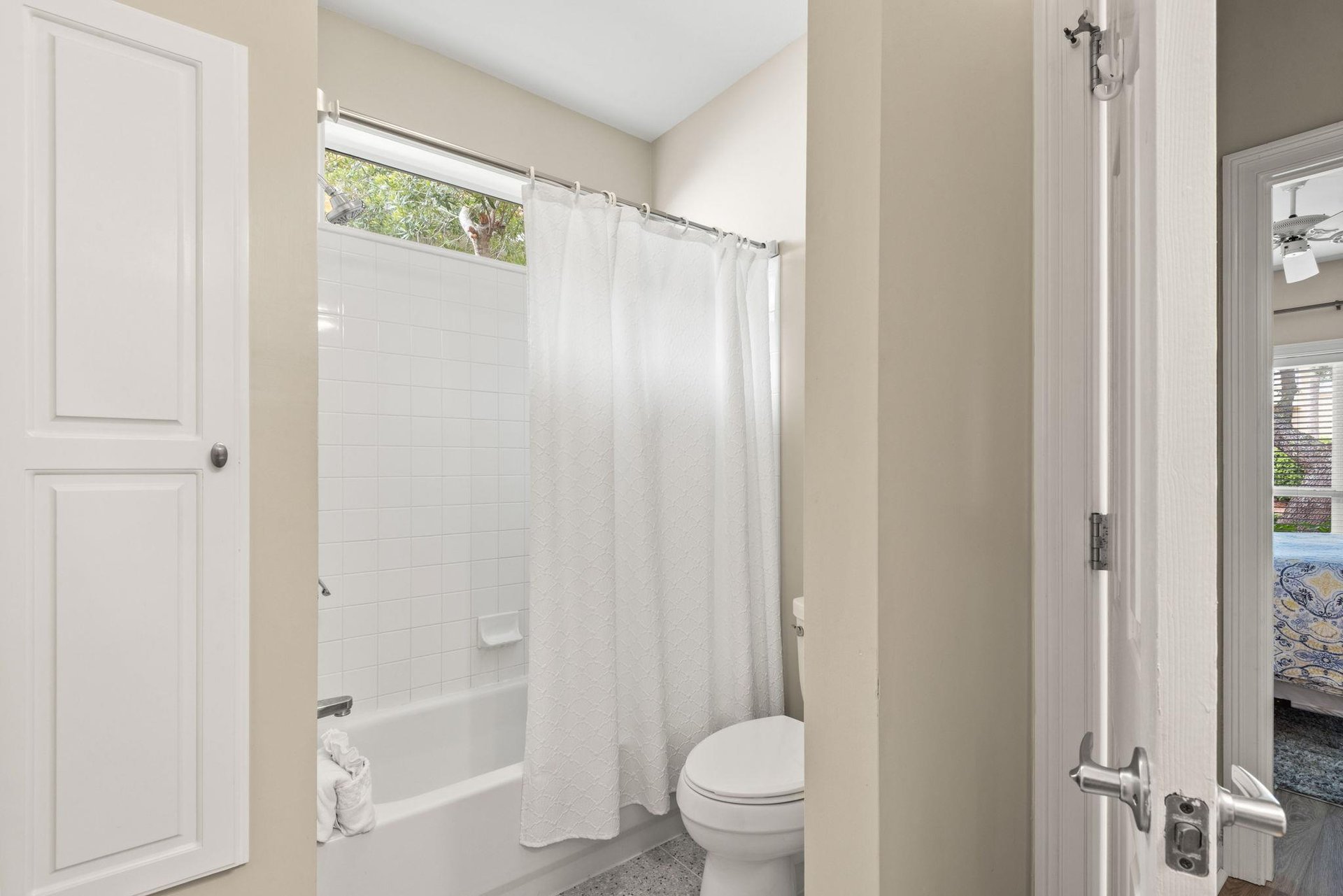 The bathroom features a refreshing showertub combo with crisp white tiling, soft natural light from above.