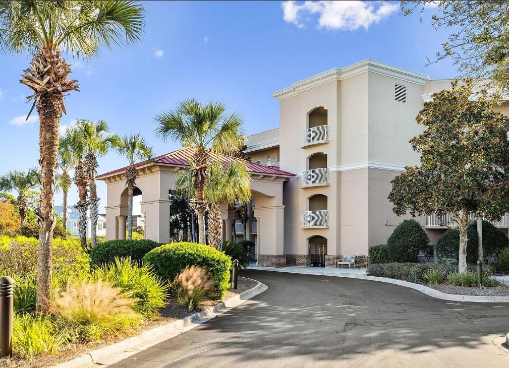 A welcoming property nestled among lush palm trees and manicured landscaping, featuring Mediterraneaninspired architecture with a covered entrance and multiple balconies overlooking beautifully maint