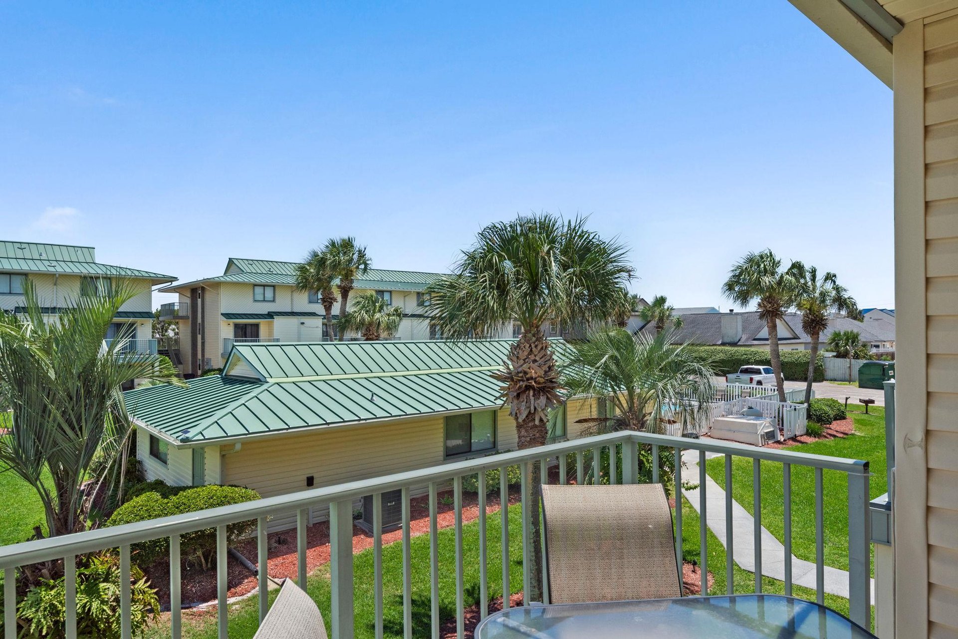 The property sits within a peaceful coastal community, surrounded by lush palm trees and neighboring properties with distinctive green roofs under bright blue skies.