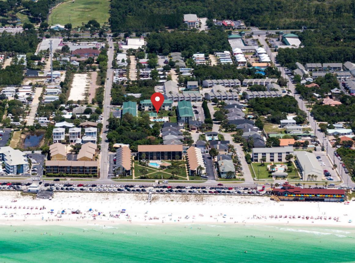 An aerial view of a pristine beachfront neighborhood, where white sand meets crystalclear turquoise water and lush greenery surrounds the community.
