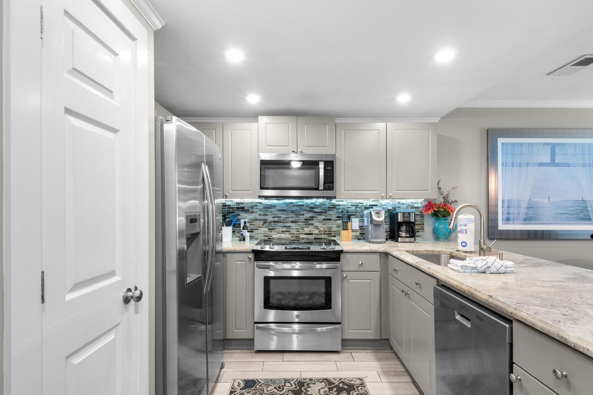 A bright, wellappointed kitchen with coastal flair—stainless steel appliances, a mosaic tile backsplash in cool blues, and plenty of counter space for making memories.