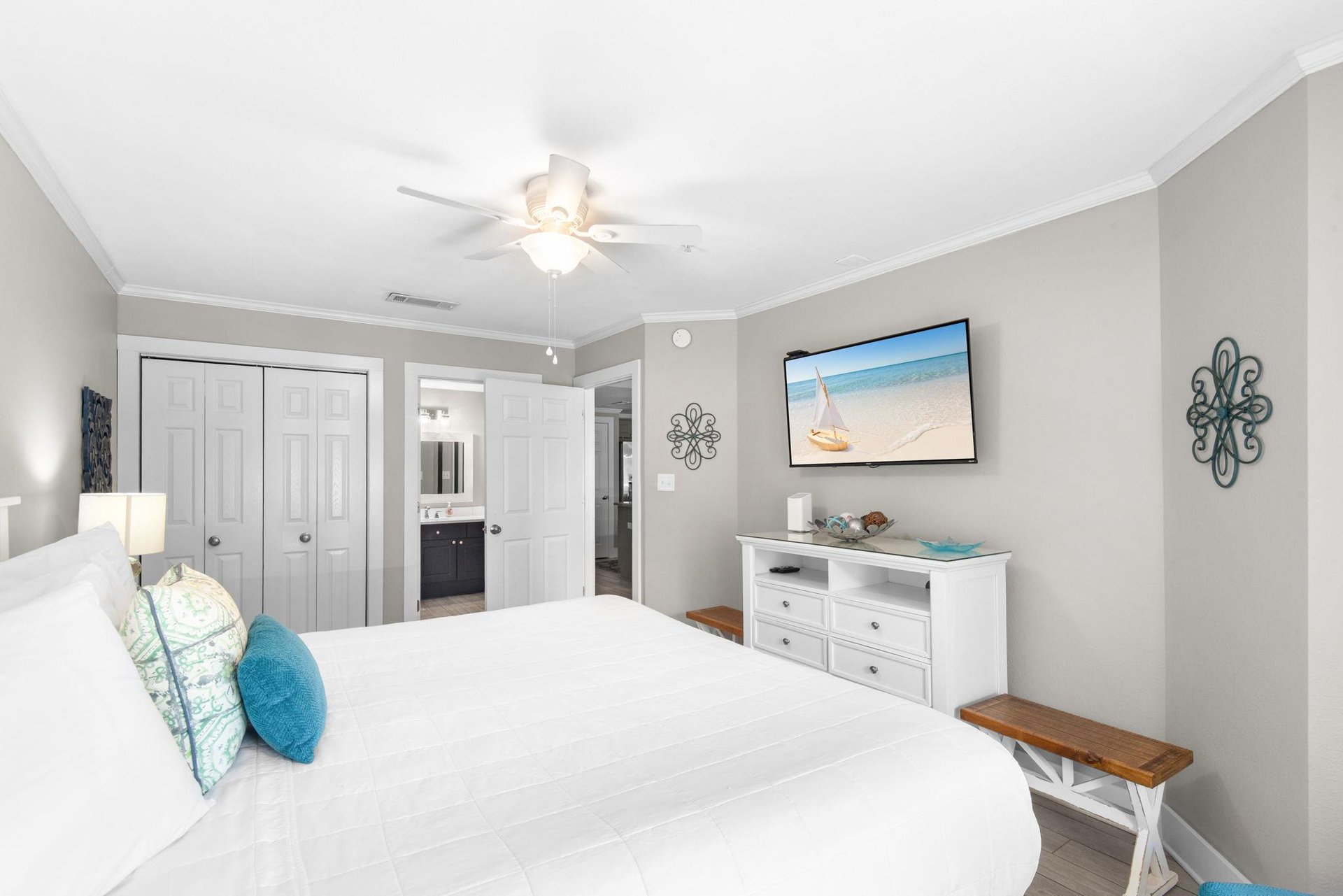 Relax in your peaceful bedroom with plush white linens, coastal accents, and a ceiling fan to keep you cool on warm evenings.