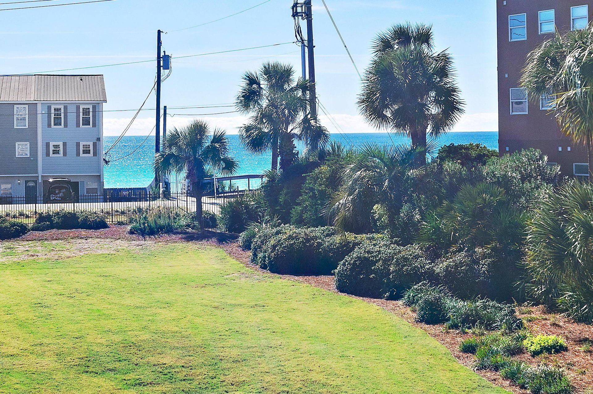 Coastal property surrounded by lush landscaping and palm trees, with the turquoise ocean visible just beyond nearby buildings—a serene beachside setting.
