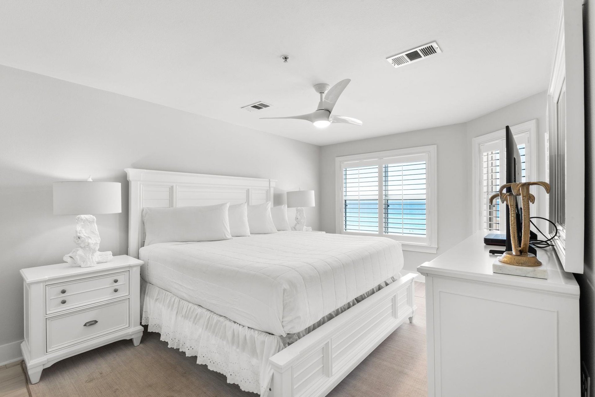 Drift off in this serene coastal bedroom with crisp linens, gentle sea breezes from the ceiling fan, and peaceful ocean glimpses through plantation shutters.