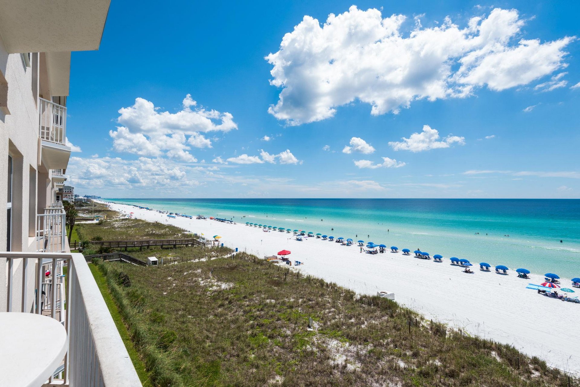 Pristine white sand stretches along turquoise waters, with colorful umbrellas dotting the shore beneath soft clouds and endless blue sky—your perfect beach escape awaits.