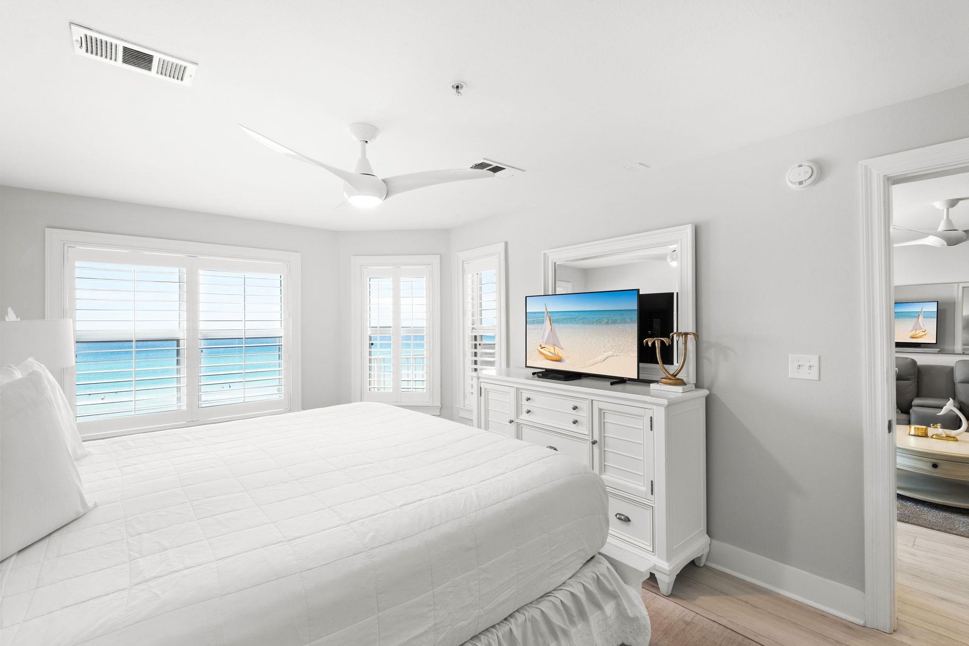 Wake up to stunning ocean views framed by bright shuttered windows in your serene coastal bedroom, complete with a gentle ceiling fan and beachinspired touches.