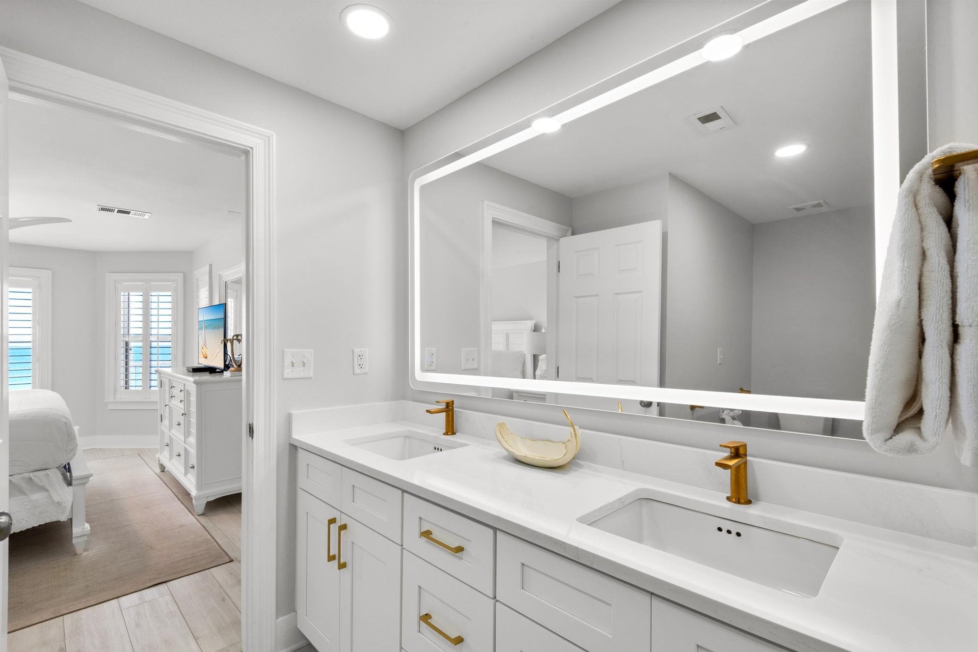 Step into your elegant ensuite bathroom where modern gold fixtures gleam against pristine white surfaces, and a spacious double vanity offers you both style and convenience for your morning routine.