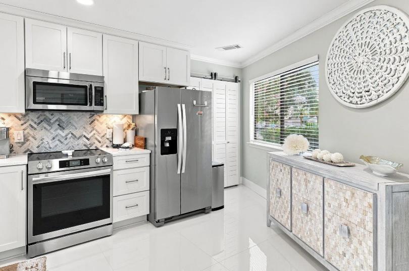 Bright modern kitchen featuring stainless appliances, herringbone backsplash, and coastal touches. Natural light floods through plantation shutters, ideal for morning coffee and vacation meals.
