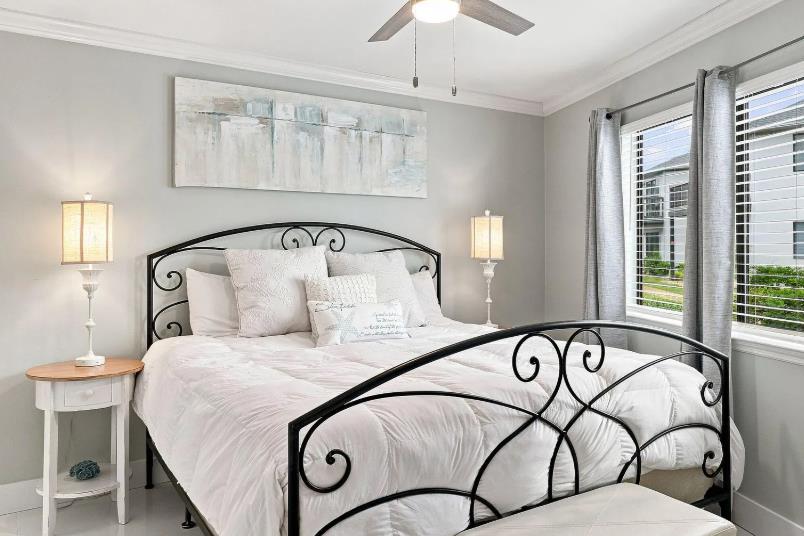 Primary Bedroom  Sink into this plush bed beneath a gentle ceiling fan, where soft gray walls and natural light through the window create your peaceful retreat.