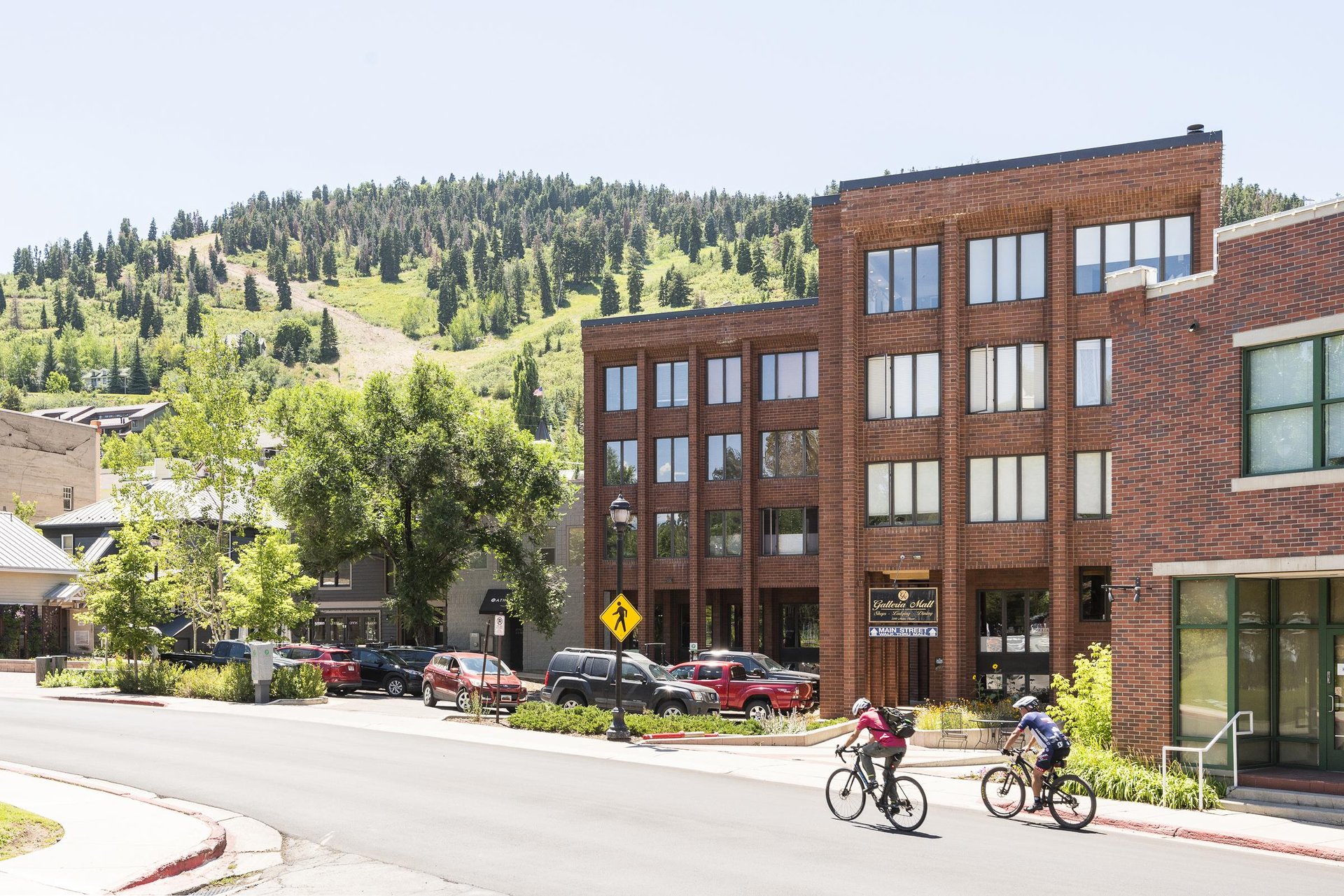 Two mountain bikers make their way up Swede Alley with Galleria in the background on a sunny summer day, green mountainside