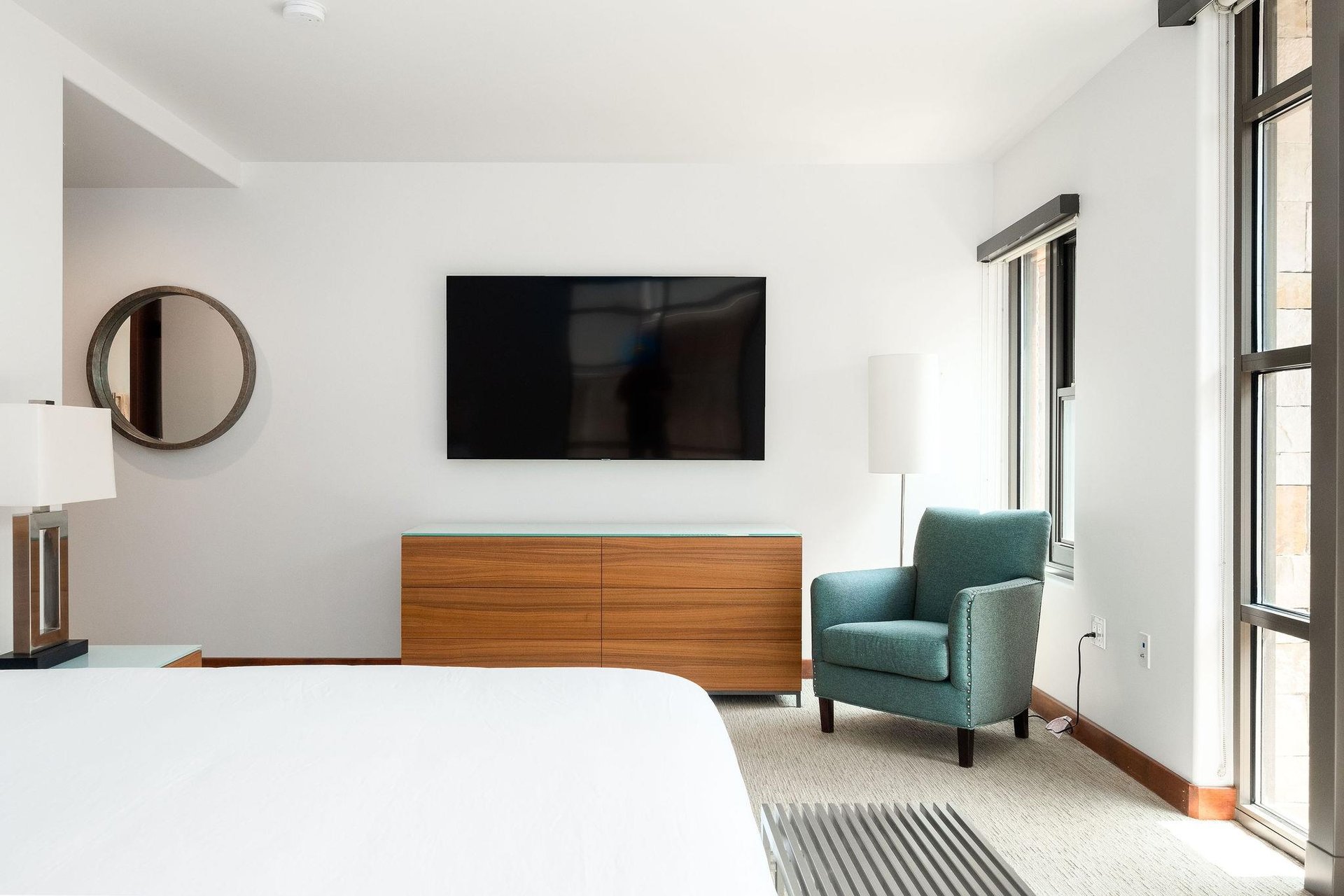 65 flat screen TV in the main bedroom over the glass topped wooden dresser and a splash of color with a blue accent chair
