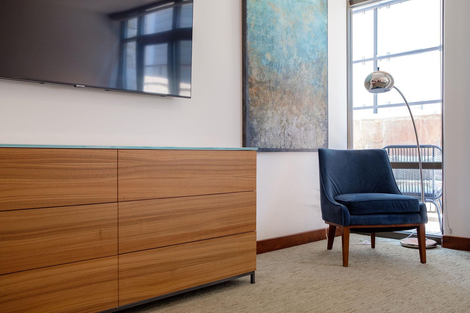 55 Flat screen TV in the guest bedroom with beautiful deep blue accent chair beneath a chrome finish floor arc lamp