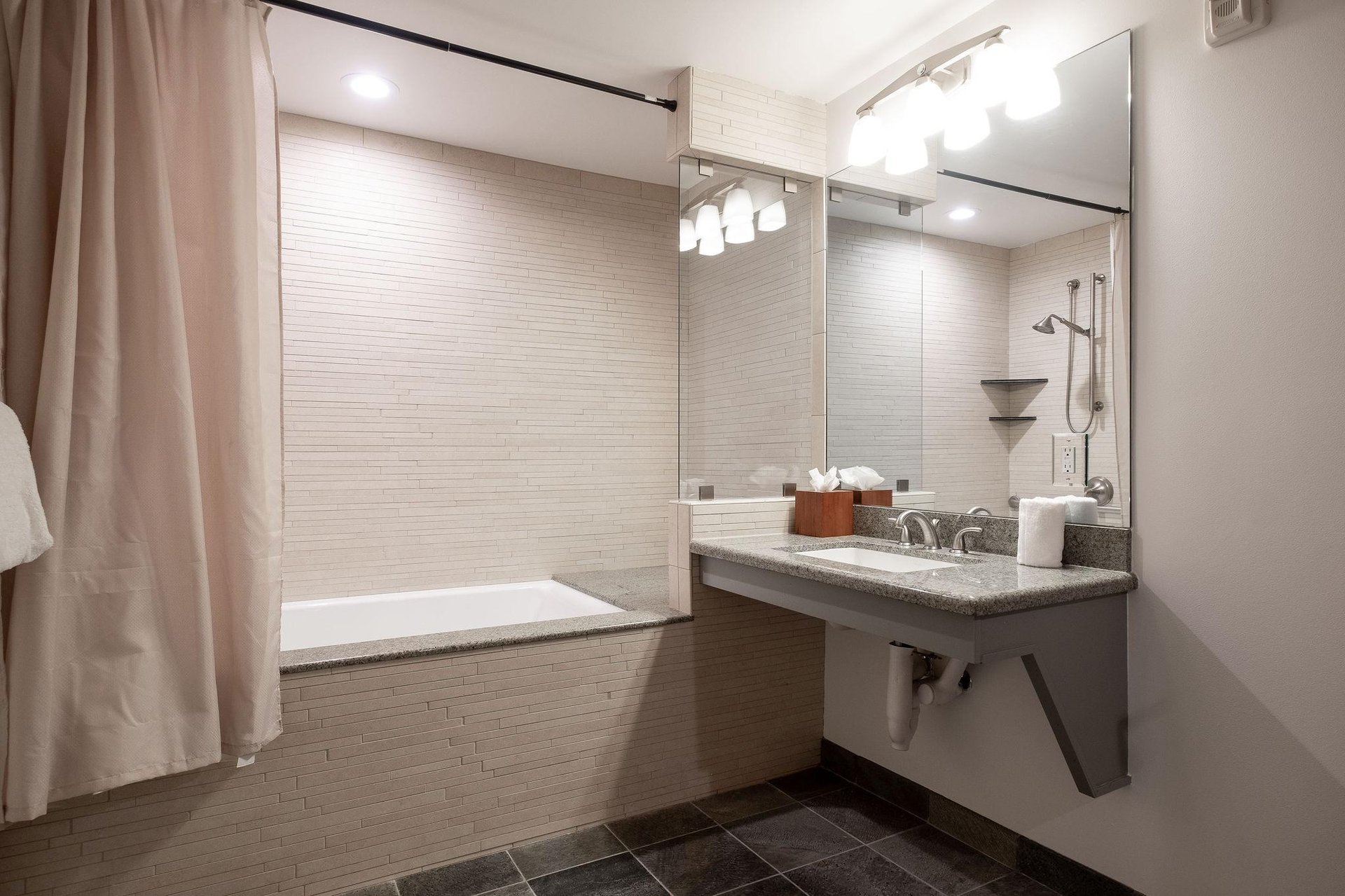 Full guest bathroom with granite floating vanity and tiled step in tubshower combo