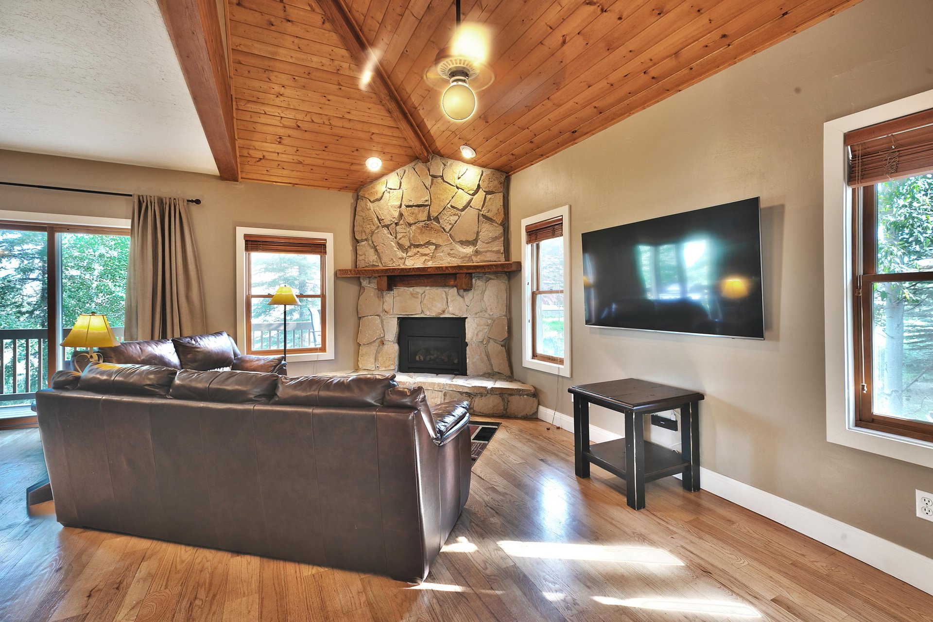 Living room with 65 wall mounted flat screen TV, wood beam vaulted ceiling, flagstone fireplace wall