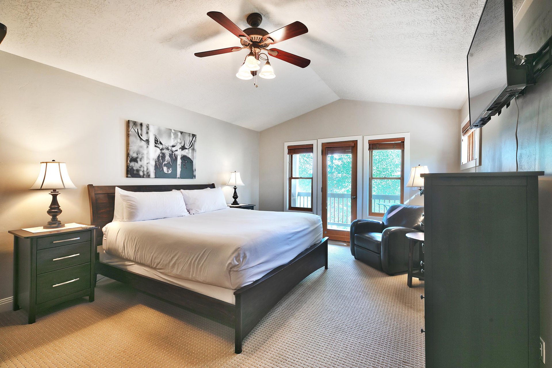 Main bedroom suite, glass patio door to private deck, vaulted ceiling and wooden blade ceiling fan, white duvet and king bed