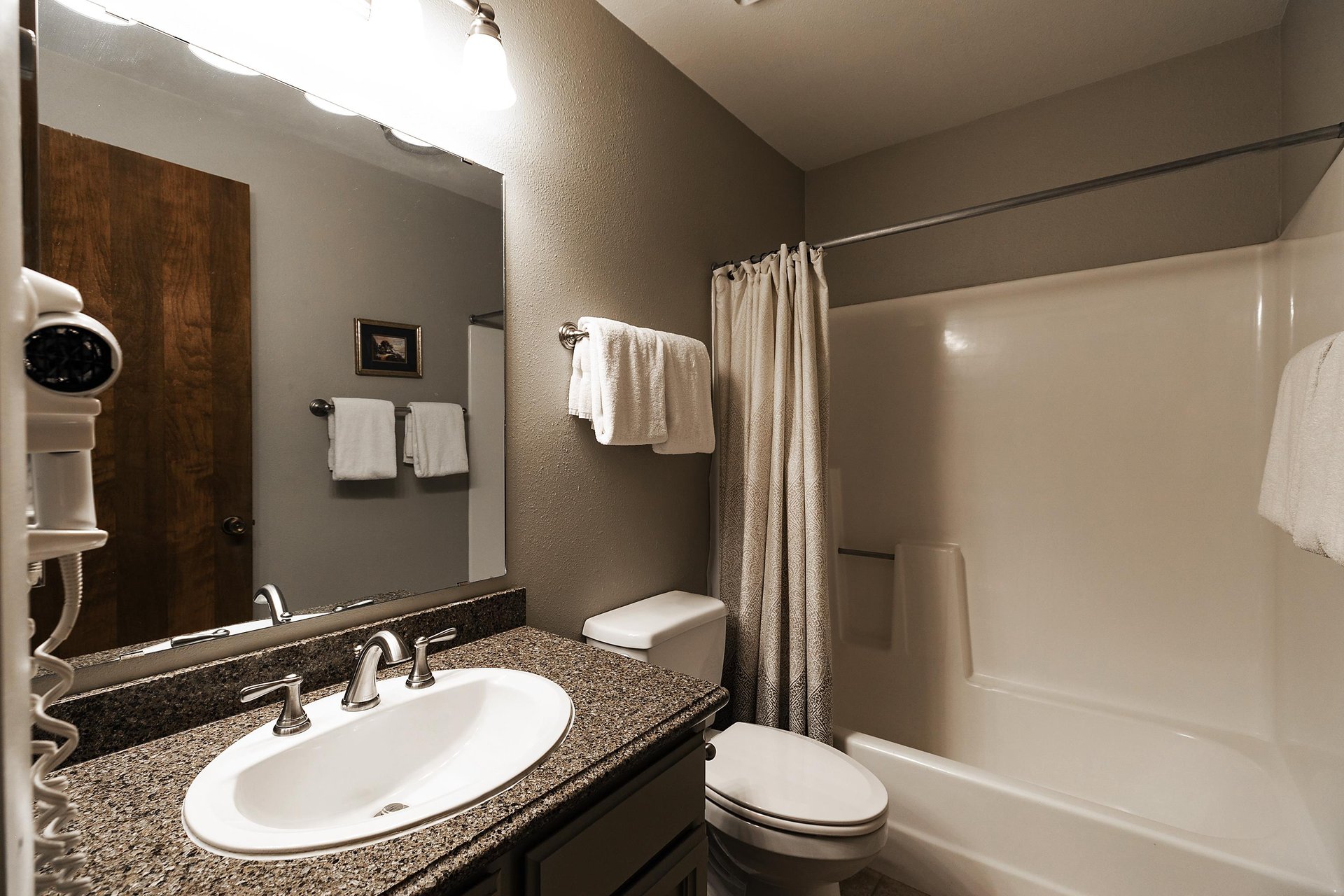 Shared guest bathroom includes dark granite countertops and a bathshower combination with a shower curtain