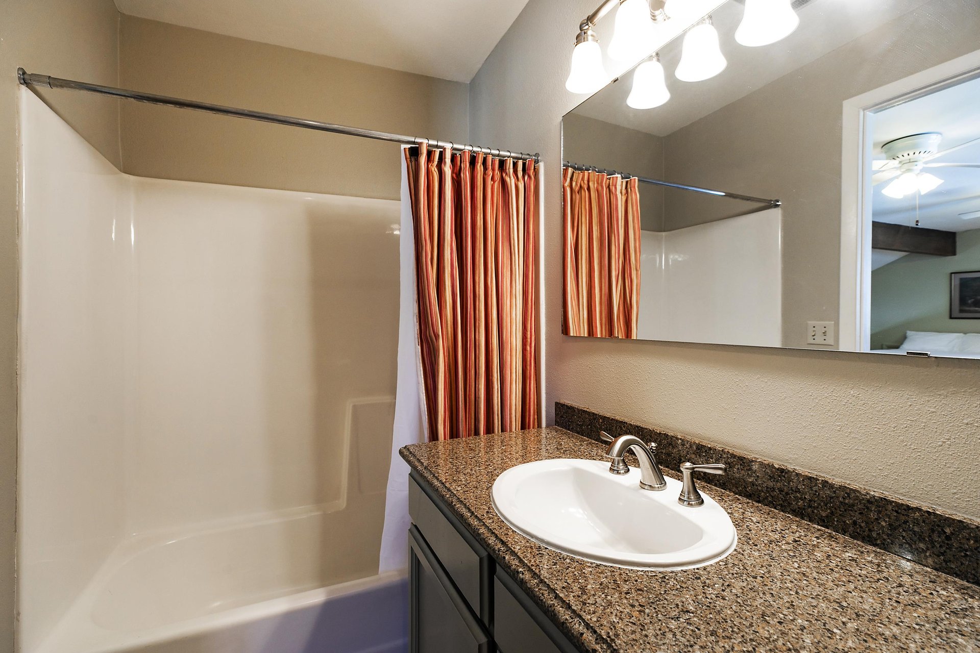 Loft bathroom has dark granite countertops and a bathshower combination with a burnt orange shower curtain