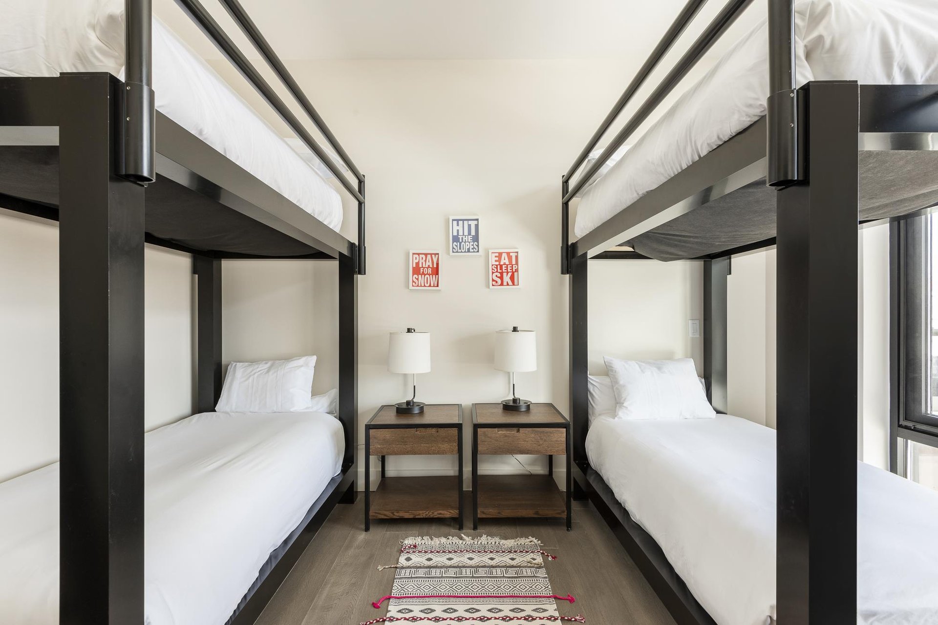 Double bunk room with wooden side tables, hardwood floors and rug runner