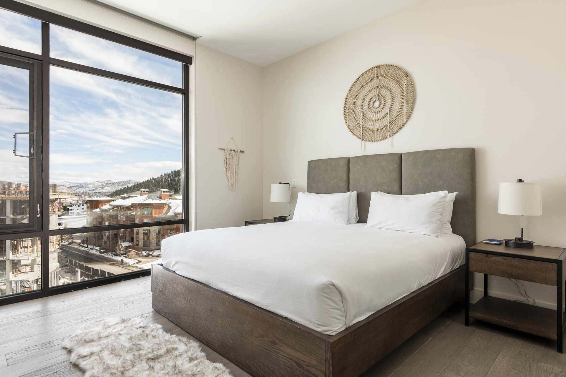 Guest bedroom with wood platform bed, suede headboard and stunning window walls with views of the resort plaza