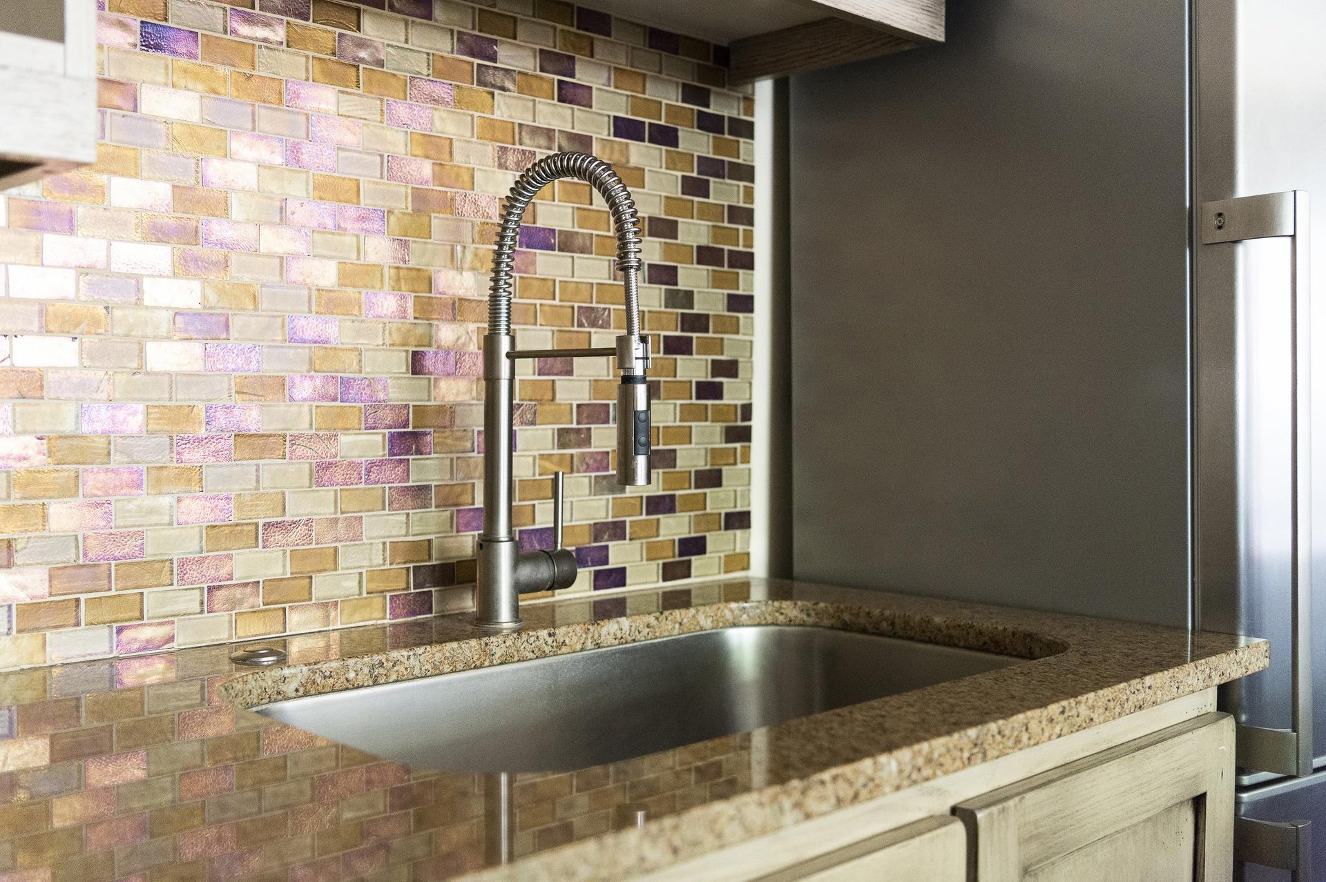 Iridescent tiled backsplash behind the chrome kitchen sink, granite countertops