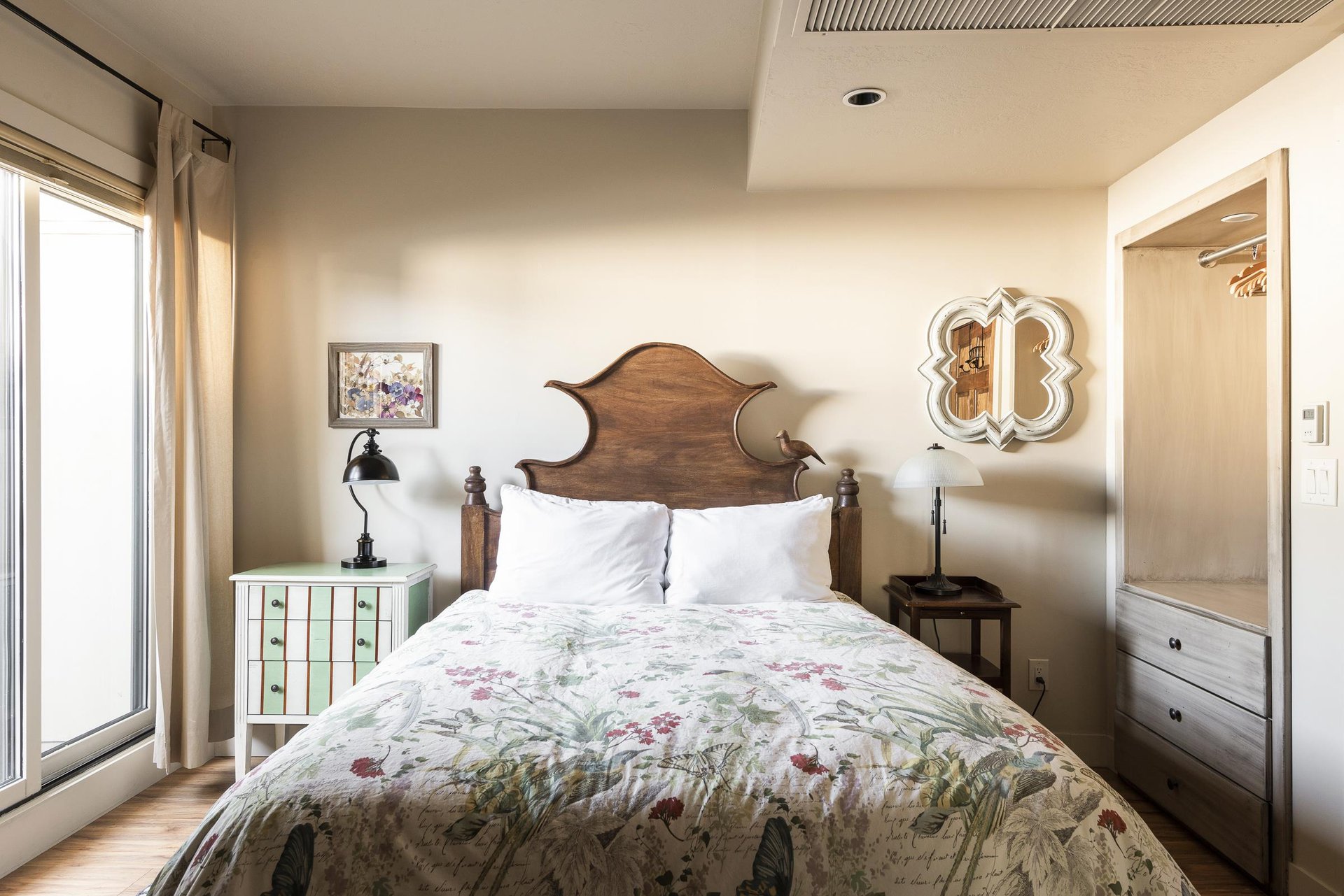 Comfortable queen bed in the bedroom with striking decorative wooden headboard with bird, window wall for abundant natural light and build in wall closet and dresser set