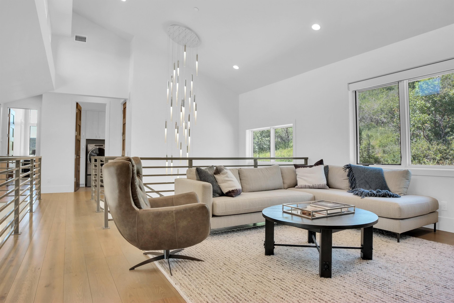 Vacation rental second living room with white walls, recessed lighting, striking chandelier, and neutral toned furniture.