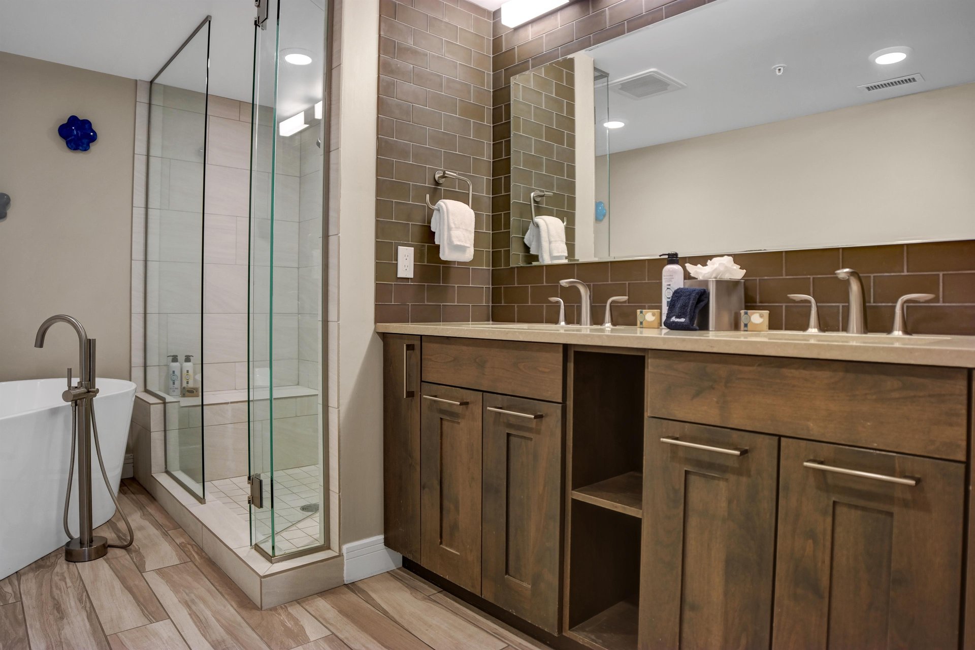 Beautiful wood vanity with double sinks and lightcolored tile walkin shower with glass surround.