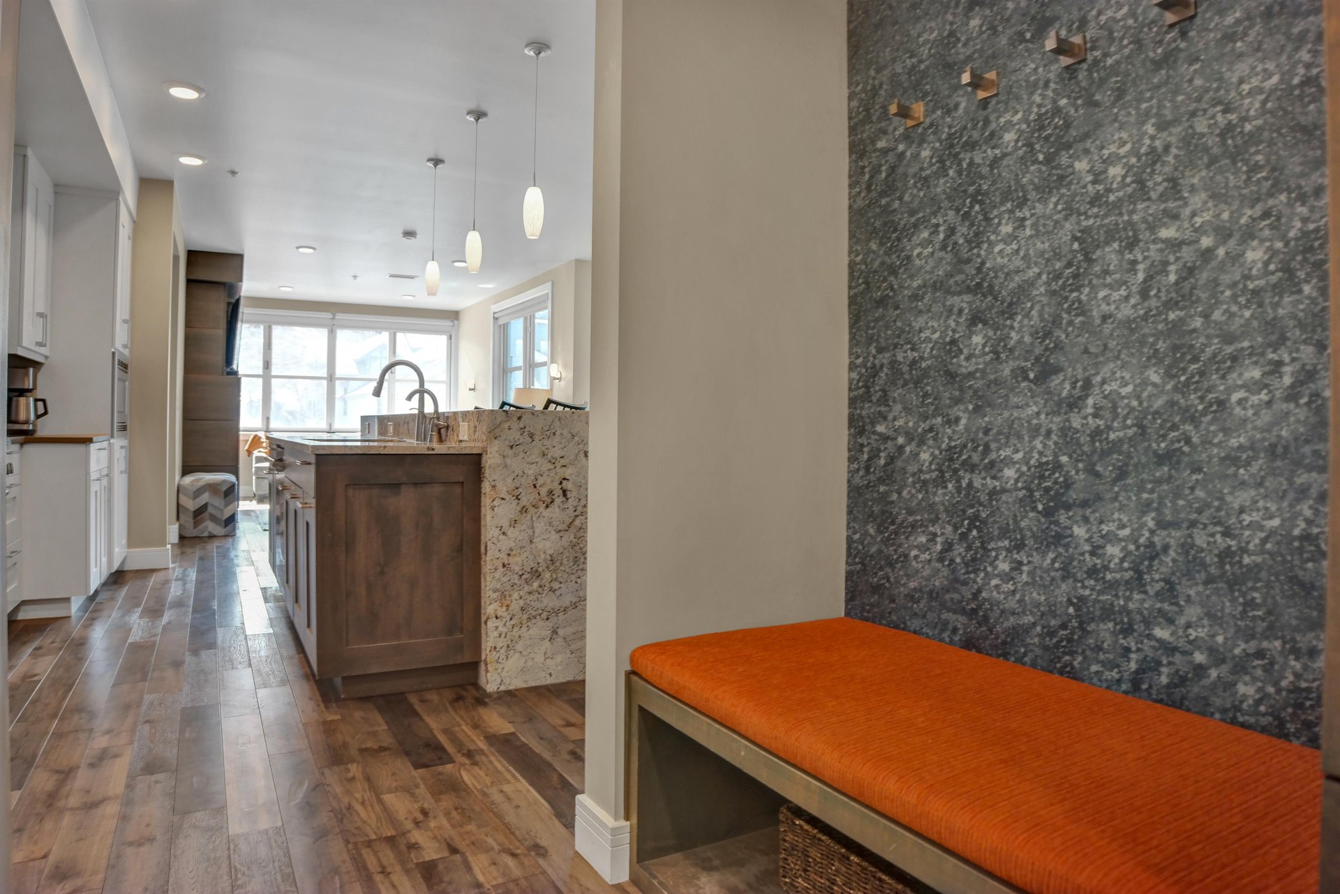 Entry bench with orange cushion and grey wall with hooks to hang jackets from.