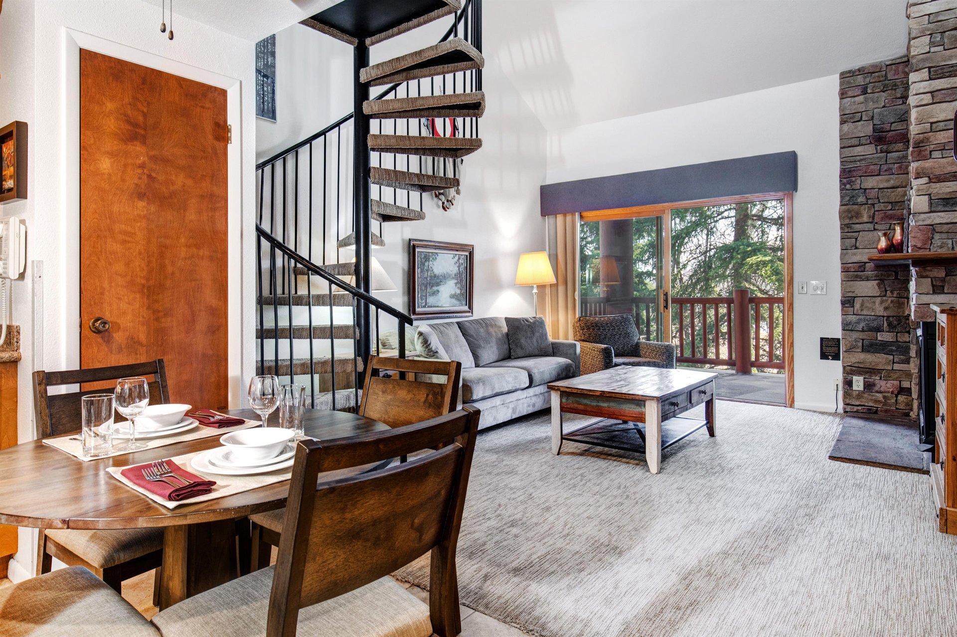 Open concept dining room and living room with a spiral staircase made of iron and wood, white walls and sliding glass doors.