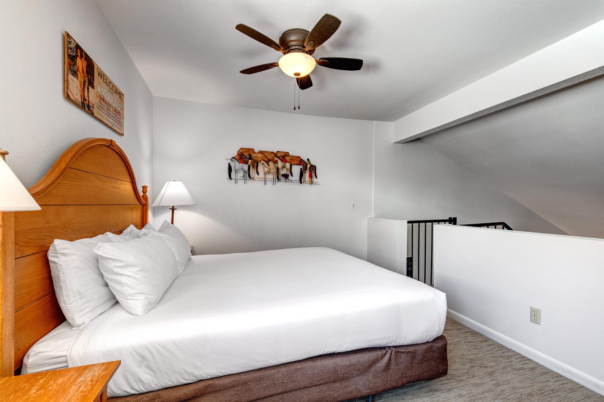 Snow Flower 31s loft with a king size bed with crisp white linens, night stands with lamps, stair entry, and picture on wall.