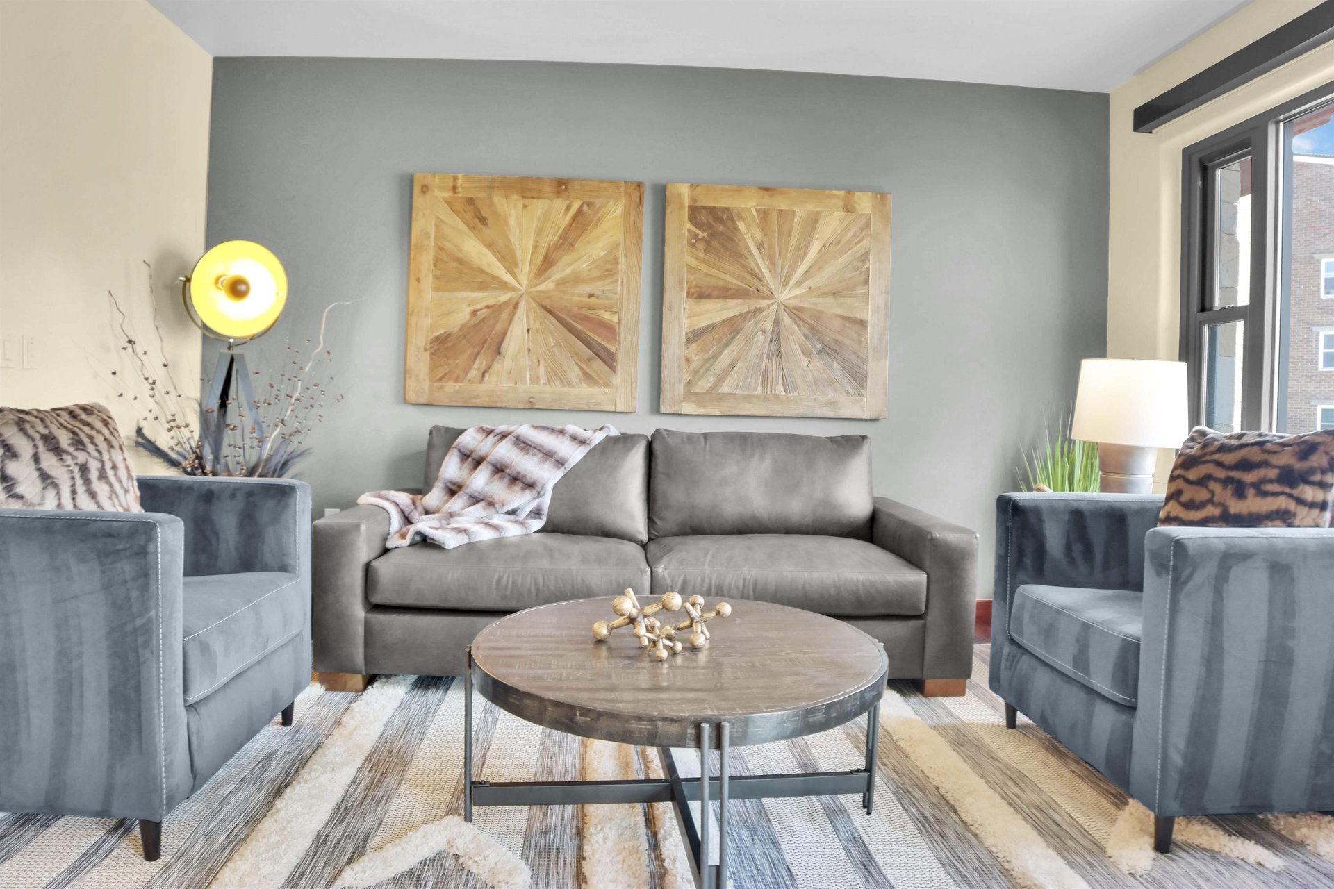 Lowell 304s living room has grey couch, loveseat, and chair, and two warm wood art pieces hung on the wall behind the couch.