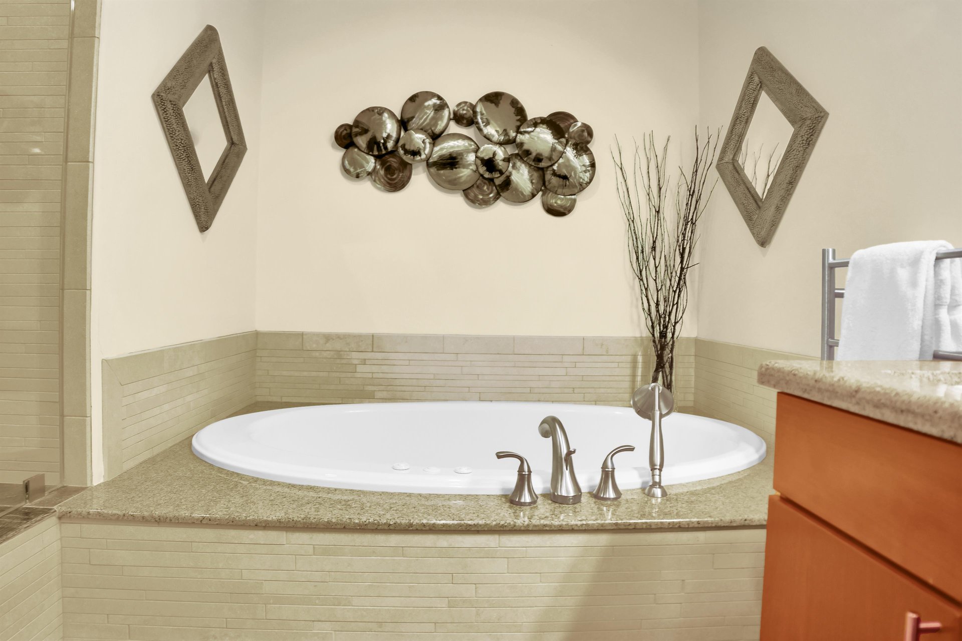 A built in deep soaker tub with cream tile surround, and bubble art and two decorative mirrors on the wall.