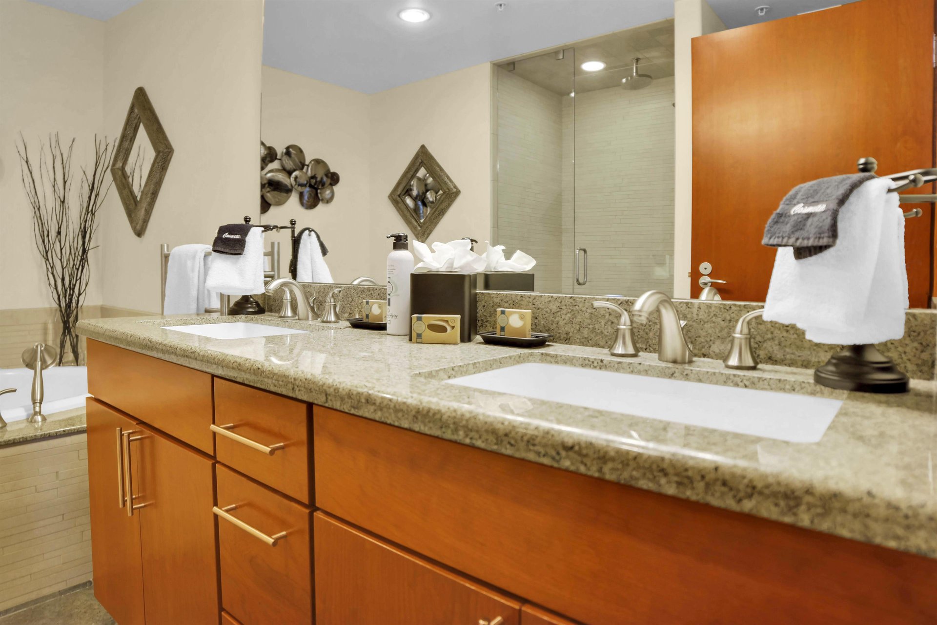 Two sink vanity with warm wood cabinets, light color countertop, large mirror and Park City Lodging toiletries.